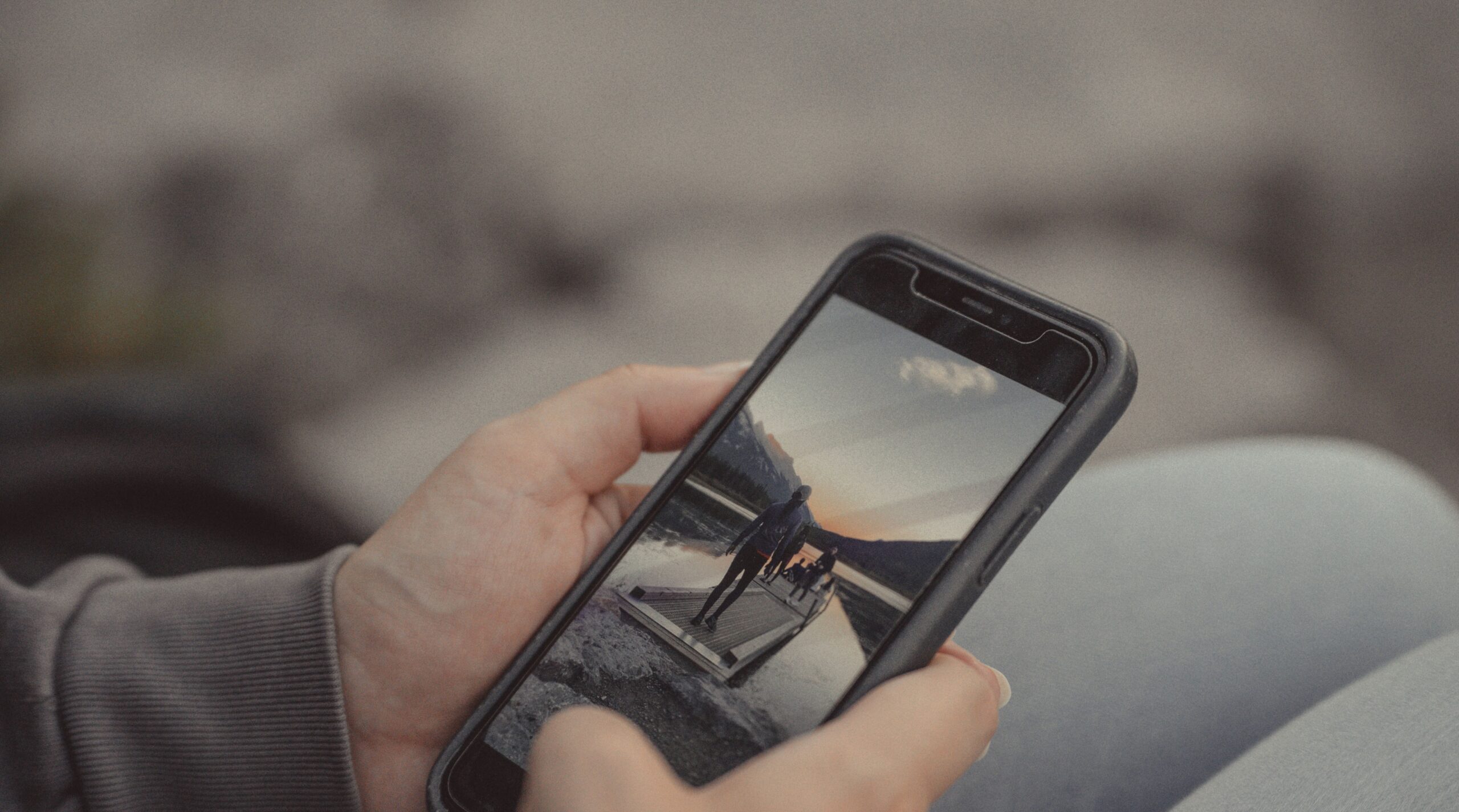 Close-up of hands holding a smartphone showing a mountain scene, captured outdoors in Banff.